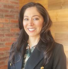 woman with long dark hair, wearing a colorful shirt and black jacket